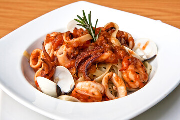 Delicious seafood pasta, clams, octopus and tomatoes served in a white plate on wooden table