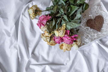 Bouquet of dry roses and a chocolate heart on a white sheet background, top view. Romantic vintage concept