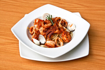 Delicious seafood pasta, clams, octopus and tomatoes served in a white plate on wooden table