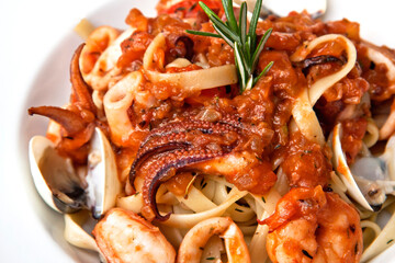 Delicious seafood pasta, clams, octopus and tomatoes served in a white plate on wooden table