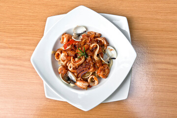 Delicious seafood pasta, clams, octopus and tomatoes served in a white plate on wooden table