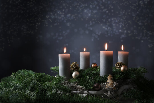 Fourth advent with four burning candles on fir branches with Christmas decoration against a dark grey background, copy space