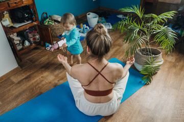 Young mother sitting on the floor, enjoy meditation do yoga exercise at home with his little...