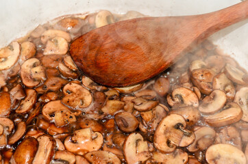 Close-up of a wooden spoon and mushrooms in a steaming pan