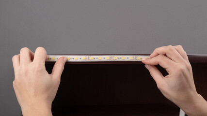 the master glues the LED strip into the niche of the shelf from the cabinet.installation of diode...