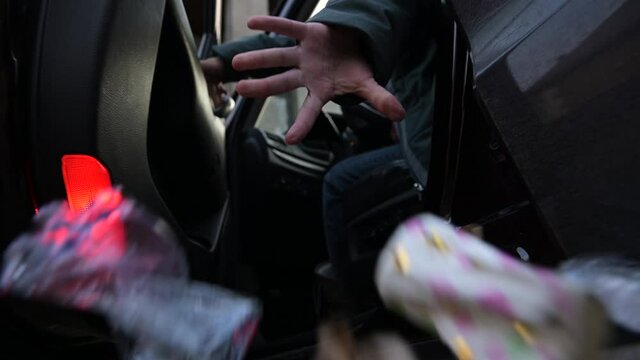 Garbage is flying out of the opened car door. The woman opens the door and throws the accumulated rubbish into the street. Slow motion