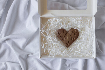 Heart shaped chocolate in a white box on the white sheet background, top view. Valentine's Day...