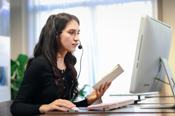Young beautiful female with headphones working at call center service desk consultant, talking with...