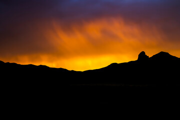 Vivid Sunset Over Black Mountain Ridgeline Silhouette Through Rain in Desert