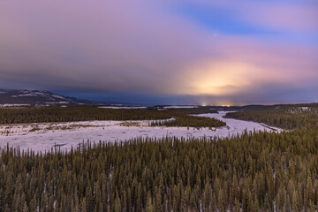 Winding Yukon River near Whitehorse, Yukon Territory at sunset in the winter time with stunning wilderness woods, forest and clouds.