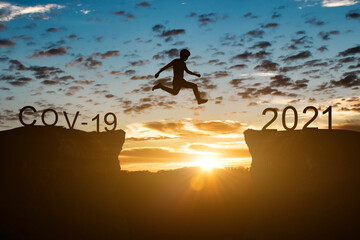 Happy new year 2021 concept. Silhouette of man jump on the cliff between 2020 (covid-19) to 2021 years over sunset or sunrise background.