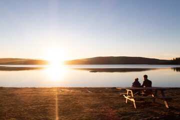 Couple sitting at a picnic table and admiring the sunset over the lake Touladi in the Temiscouata national park, Canada