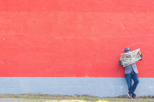 Man is reading newspaper on a red wall with much copy space