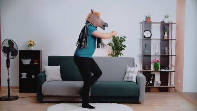 A man in a horse mask is dancing merrily in the room.
