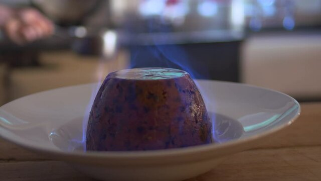Chef pours flaming whiskey flambe liquid over Christmas puddy cake desert