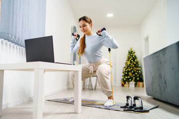 Front view on young caucasian woman at home watching online video on laptop computer for training - Girl using rubber tubes resistance bands for workout in room - health and fitness concept copy space