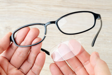 Hands hold eyeglasses with broken rim and fallen out lens. Spectacles with cracked black eye wires...