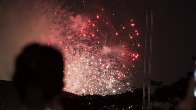 Female Spectator Taking Photo Of Beautiful Fireworks Over Marina Bay (View From Padang) - Singapore National Day Celebration - rack focus, slow motion