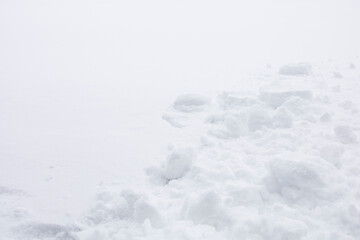 White soft and fuzzy snow in December with natural bright light. Close up pieces of pure and clean icy snow texture with part of empty smooth surface background. Winter season concept