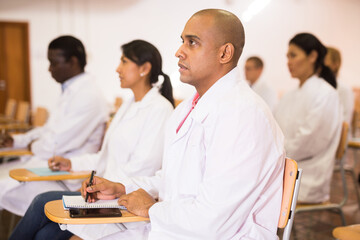 Portrait of young adult male doctor attentively listening to lecture with colleagues at medical conference