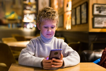 Portrait of tween boy carried away with phone while sitting at table in cafe..