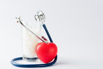 A glass full of white sugar cube sweet food ingredient and doctor stethoscope, studio shot isolated white background, health high blood risk of diabetes and calorie intake concept and unhealthy drink