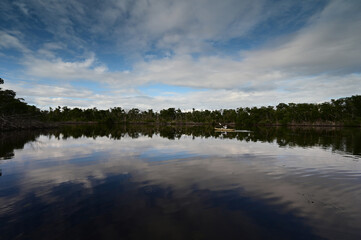 Distant kayaker in Coot Bay Pond, Everglades National Park, Florida under winter cloudscape reflected in tranquil water.