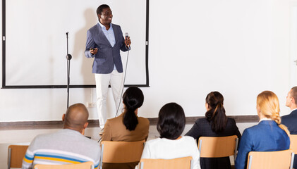 Positive African American with microphone speaking at corporate business event in conference room