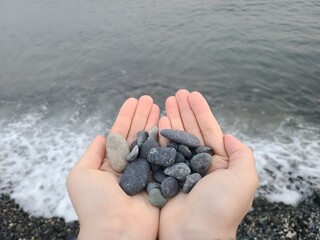 Two hands with stones against the backdrop of the waves