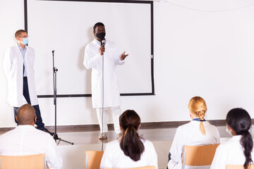 Portrait of confident successful male coach in face mask for disease protection giving speech at medical conference