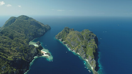 El Nido Islands at blue sea bay aerial view. Green mountain isles with tropical forest at sand beach. Wonderful seascape with greenery islets of Philippines Archipelago. Cinematic drone shot