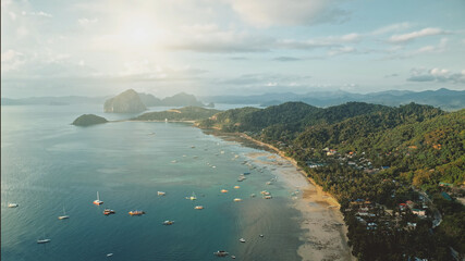 Ocean pier town aerial: sun cityscape with lot of boats, ships, vessels at waterfront. Cottages and lodges at green palm trees on hills. Water transport at tropic Filipino resort of Palawan island