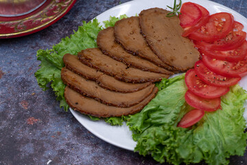 Vegan seitan roast slices with tomato slices on lettuce leaves on.white plate
