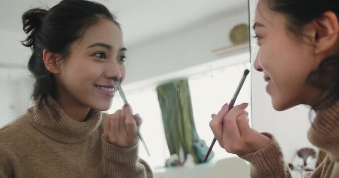 Cute Asian girl applying makeup in front of the mirror The young Chinese girl is very happy looking at her beautiful self in the mirror, full of confidence 4K beauty-conscious young people dressing