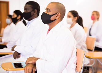 Fototapeta na wymiar Hispanic doctor wearing protective face mask listening to lecture during medical congress. Necessary precautions in public place in coronavirus pandemic