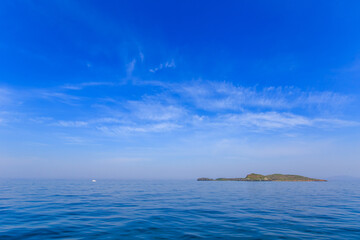 A small uninhabited green island in the middle of a calm blue sea and blue sky. Beautiful relaxation background.