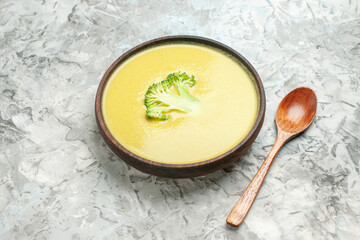 Side view of creamy broccoli soup in a brown bowl and spoon on gray background