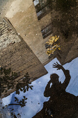 Dark silhouette of man in coat reflected in puddle