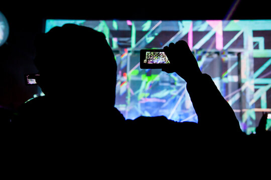 Silhouette of  man with a phone photographing a light show