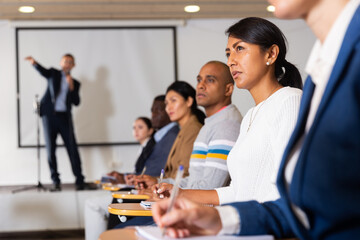 Portrait of young focused woman sitting and listening to speaker at business conference