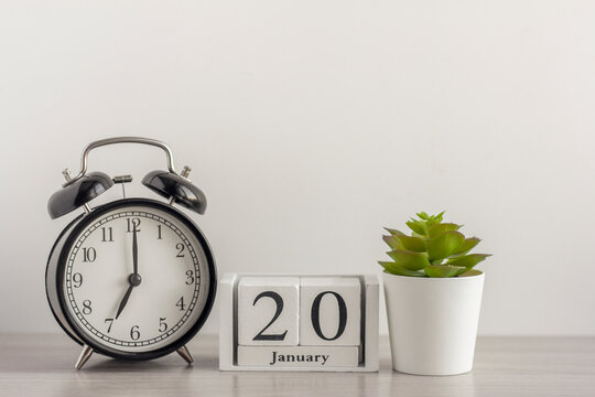 January 20 on a wooden calendar, next to a retro alarm clock and a succulent in a mini pot on a light table.One day in January.Winter day.A copy of the space.Workplace.