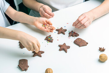 Cooking Christmas and  New Year chocolate cookies or gingerbread. Traditional festive baking, bake with kids. Mom and child hands Decorate baked gingerbread with multi-colored sweet sprinkles