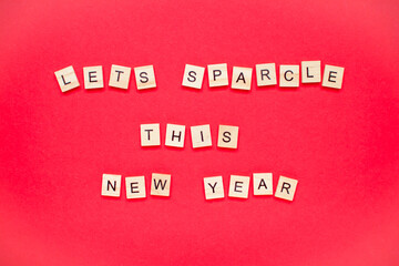 Fototapeta na wymiar Lets sparcle this new year. The inscription from wooden blocks on a bright red background. New Year.