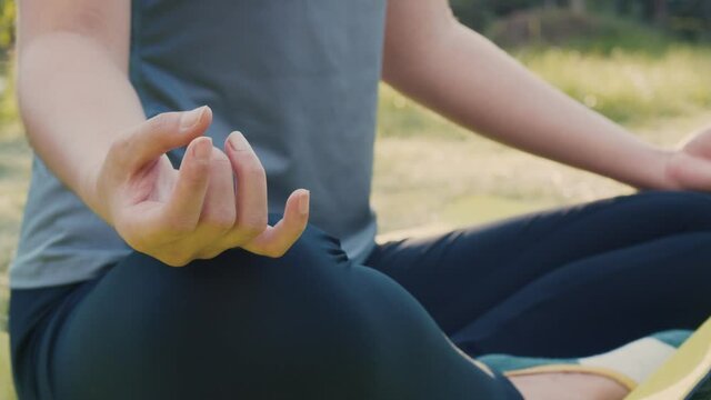 Close up of hands Asian female sitting in meditation pose position yoga pranayama balance in the beautiful the park view during sunset.