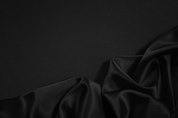 Black silk satin fabric background. Copy space for your design. Delicate wavy folds. Beautiful elegant black background.