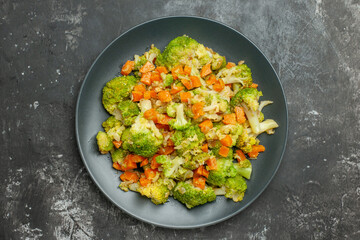 Healthy meal with brocoli and carrots on a black plate on gray background