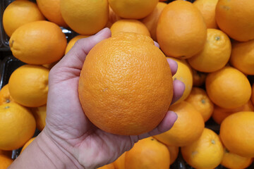 Close up hand holding a fresh orange in a grocery store.