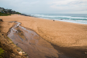 Stream Running onto Beach with Waves and Rocks in Background