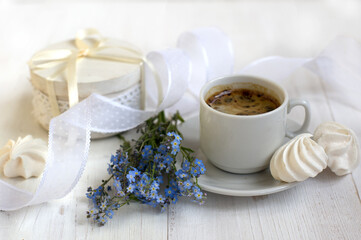 Obraz na płótnie Canvas romantic breakfast: cup of coffee, meringues, a bouquet of forget-me-nots, a white ribbon on a light background