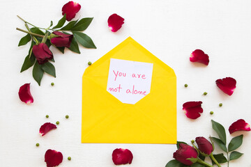 you are not alone  message card handwriting in yellow envelope with red rose flowers decoration flat lay style post card send to special on background white wooden